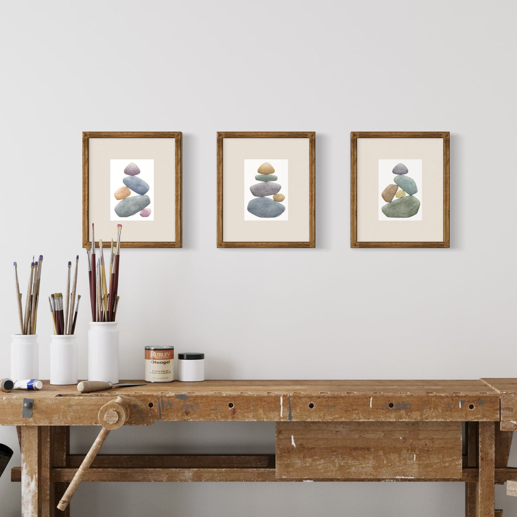Three framed artworks of stacked stones on a wall above a wooden workbench.