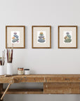 Three framed artworks of stacked stones on a wall above a wooden workbench.
