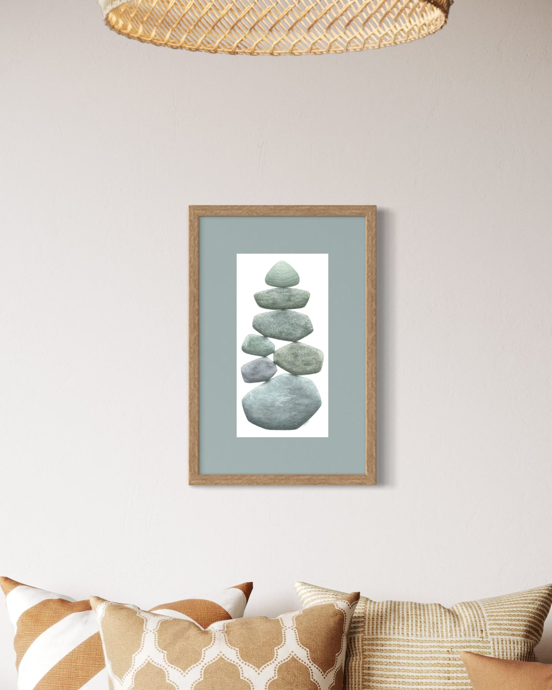 Framed artwork of stacked stones on a wall above a sofa with patterned cushions.