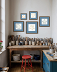 Studio with wooden workbench, pottery, and framed leaf artwork on the wall.